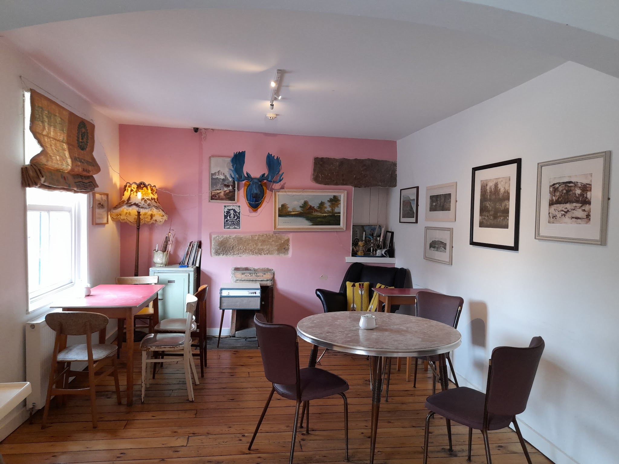 An inviting pink-walled room with books, artwork and cafe tables
